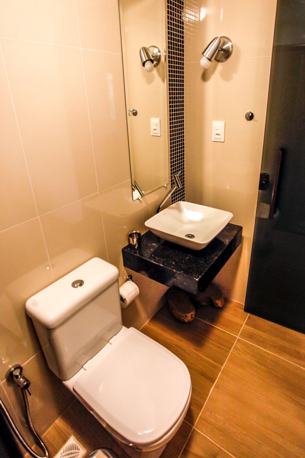 Un baño moderno con inodoro blanco, lavamanos negro y zona de ducha.