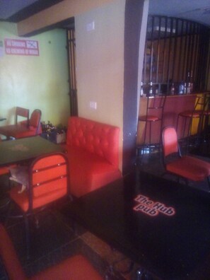 A room with a red sofa, a small table, and a chair. There is a sign on the wall and a door with a sign on it. - The Hub Guest House (Thika)