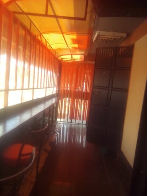 A corridor with a reflective floor, a wooden bench, and a door with a metal gate. - The Hub Guest House (Thika)