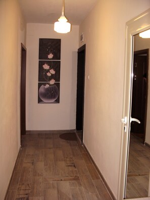 Um corredor com piso de madeira, luminária fixada na parede e uma obra de arte emoldurada retratando flores e a lua.