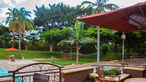 A poolside area with outdoor furniture, a red umbrella, and lush greenery in the background. - Utalii Hotel (Nairobi)