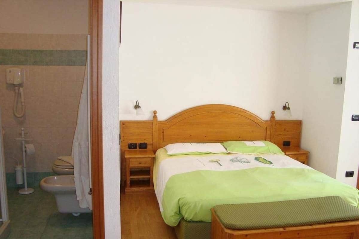 Un dormitorio con una cama de madera, ropa de cama verde, una mesita de noche y un banco de madera.