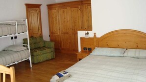 A bedroom with a wooden bed, a green armchair, a bunk bed, and a wooden wardrobe. - La Falconetta (Ayas)