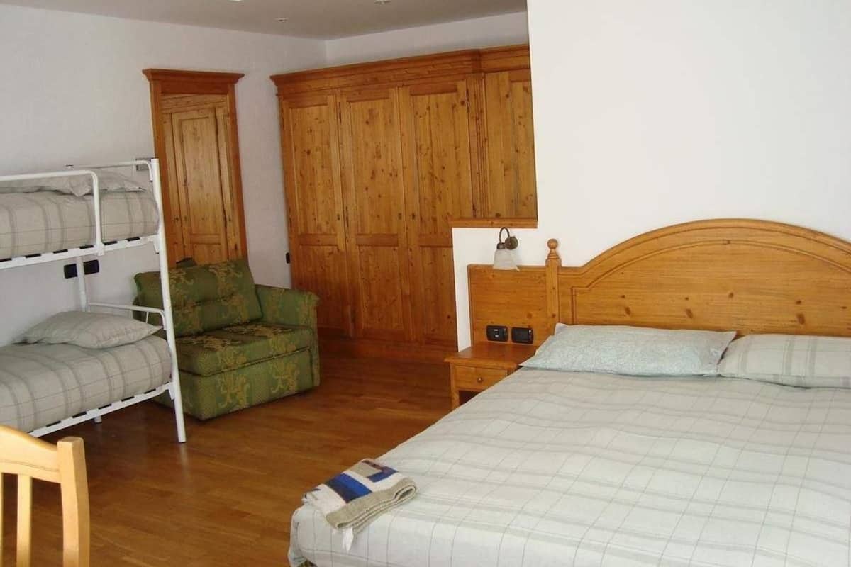 Un dormitorio con una cama de madera, un sillón verde, una cama nido y un armario de madera.