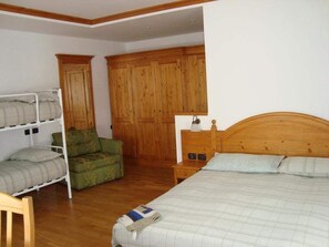 Une chambre à coucher avec un lit en bois, un fauteuil vert, un lit superposé et une armoire en bois.