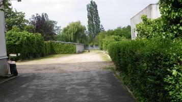 A paved driveway leading to a gated area with dense greenery on both sides.
