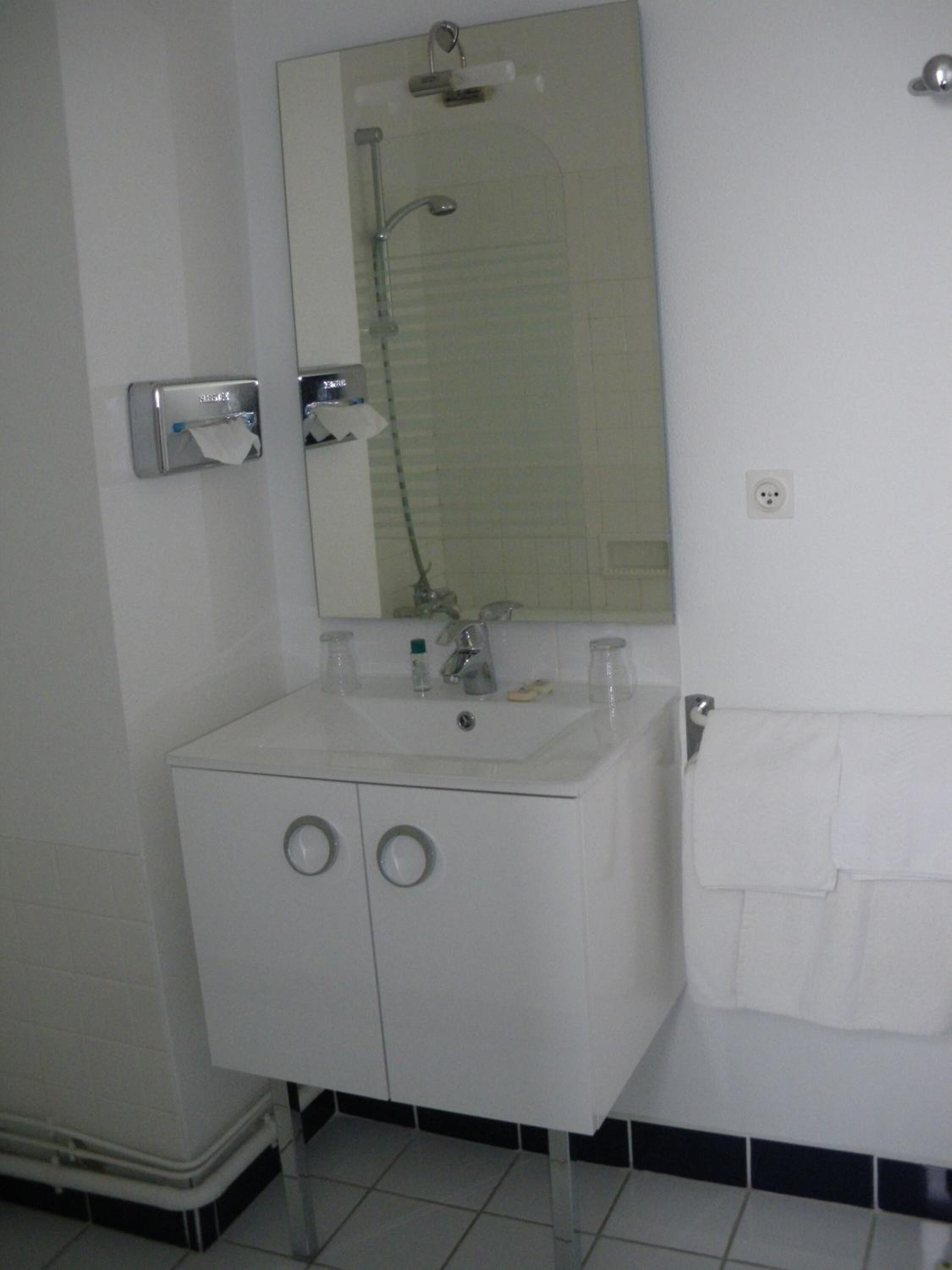 Casa de banho com lavatório branco, espelho e porta-toalhas.