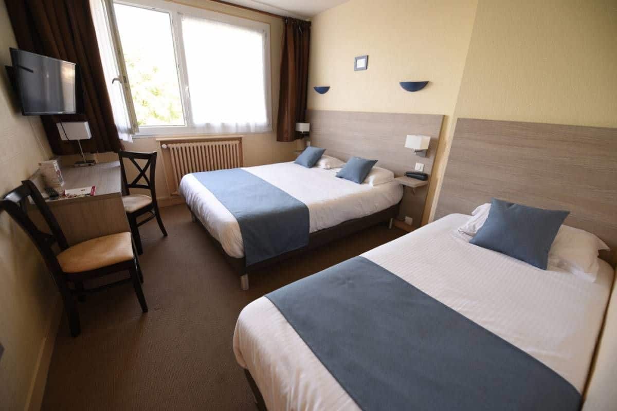 A hotel room with two beds, a desk, a chair, a TV, and a window with curtains.