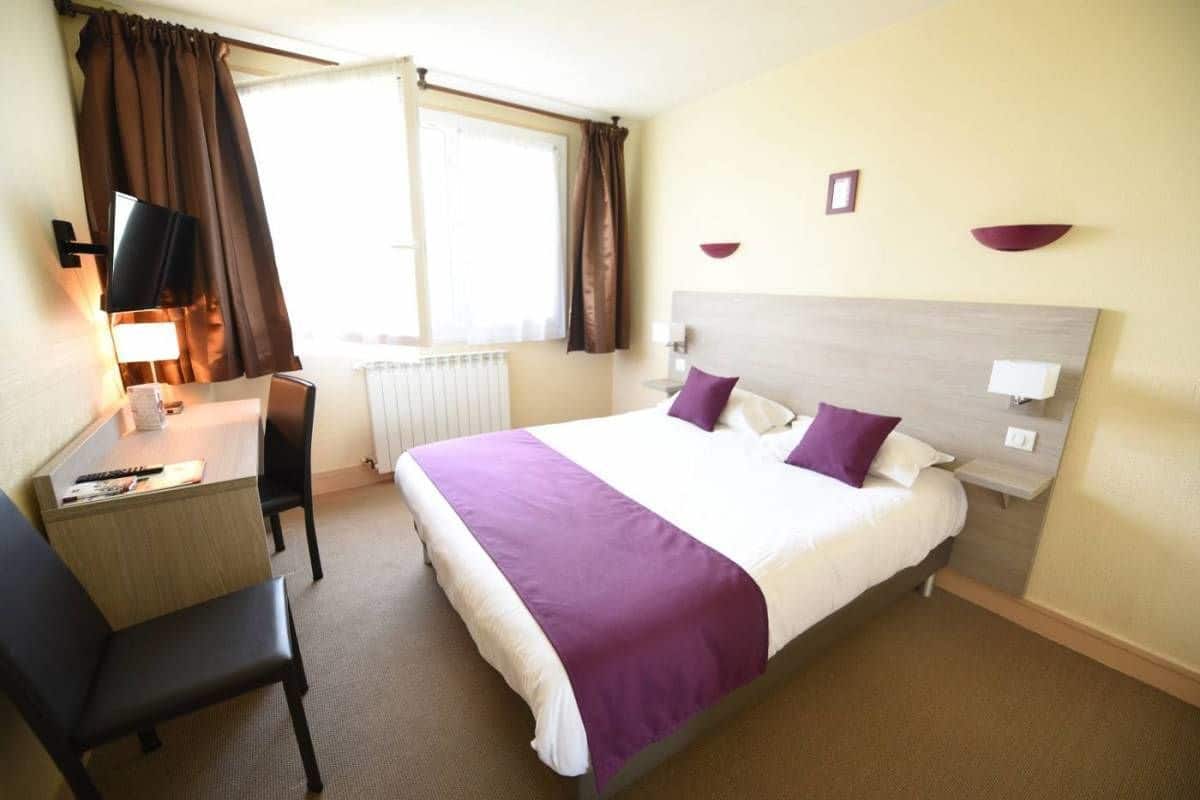 A hotel room with a bed, a desk, a chair, a television, and a window with curtains.