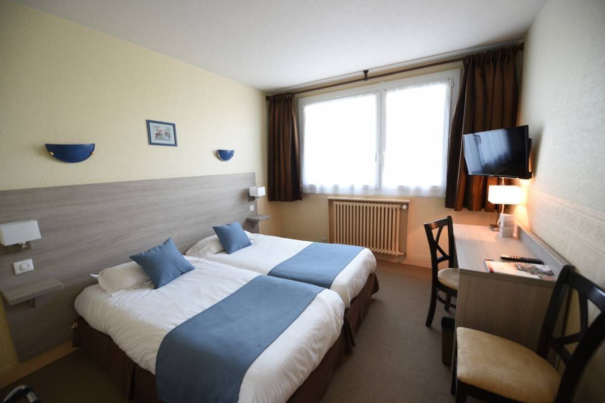 A hotel room with two beds, a desk, a chair, a TV, and a window with curtains.