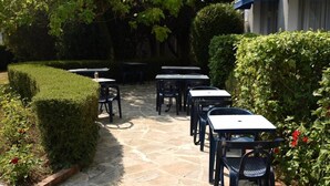 Een terras buiten met stenen vloer, tafels en stoelen klaar voor dineren.
