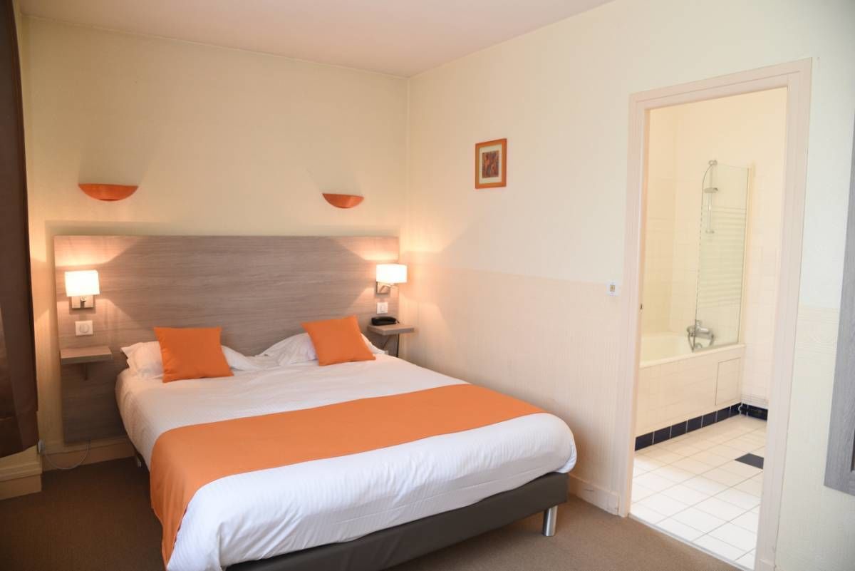 Habitación de hotel con cama, dos lámparas de noche, mesita de noche y baño con ducha.