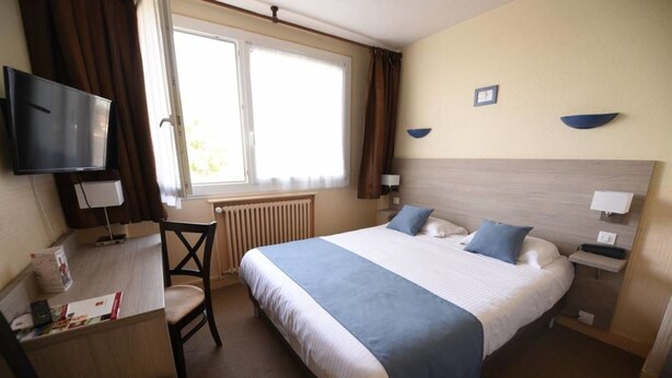 Een hotelkamer met een groot bed, een bureau met stoel, een televisie en een raam met gordijnen.
