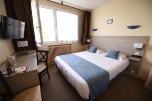 Une chambre d’hôtel avec un grand lit, un bureau avec une chaise, une télévision et une fenêtre avec des rideaux.