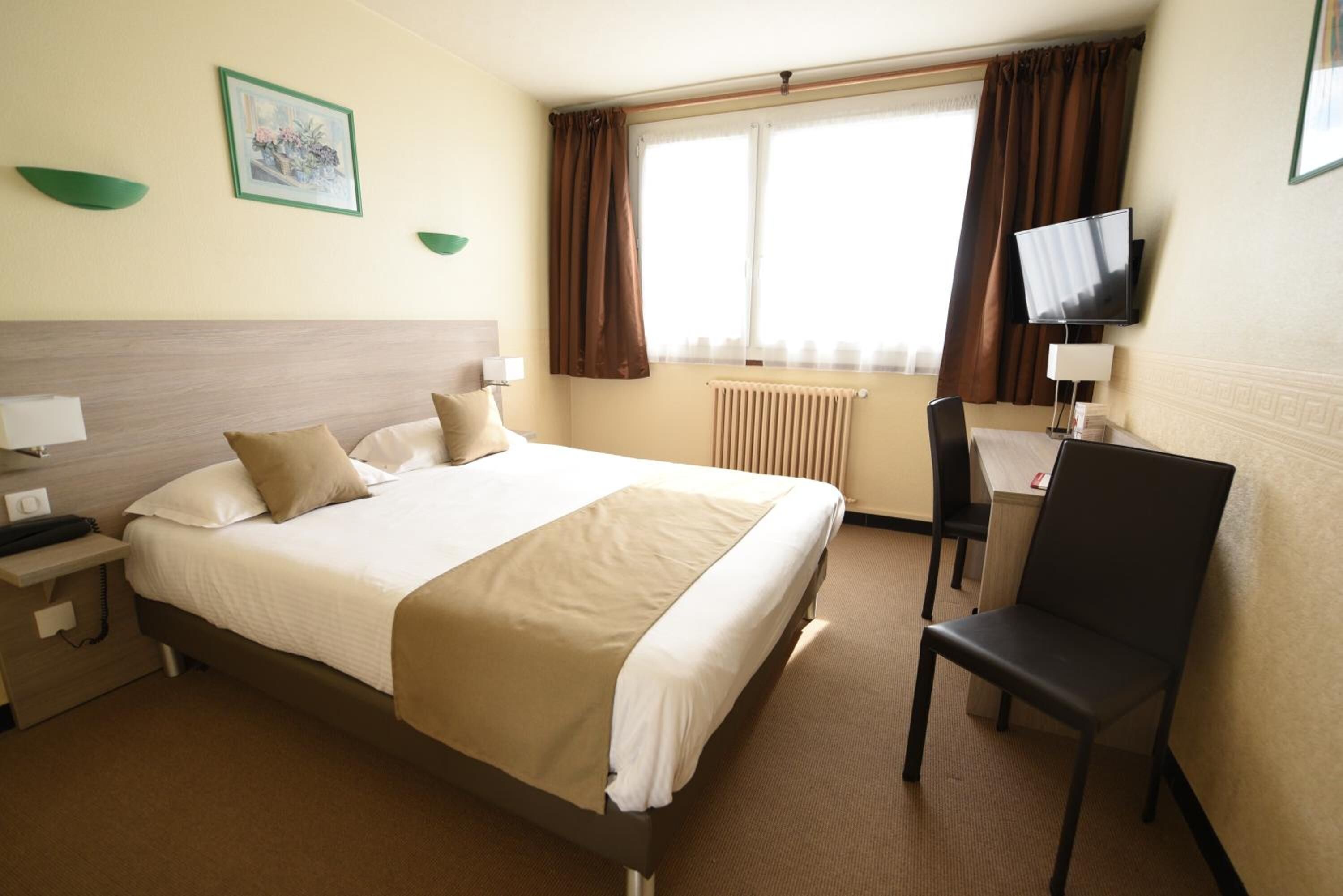 A hotel room with a bed, bedside table, chair, TV, and a window with curtains.