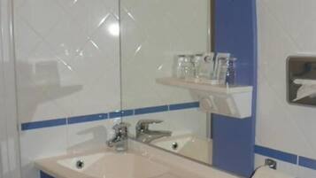Un baño con lavamanos, espejo y repisas con artículos de tocador.