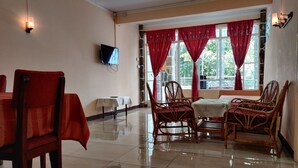 A dining area with a table and chairs, a TV mounted on the wall, and red curtains on the windows. - Pereybere Beach Apartments (Grand-Baie)