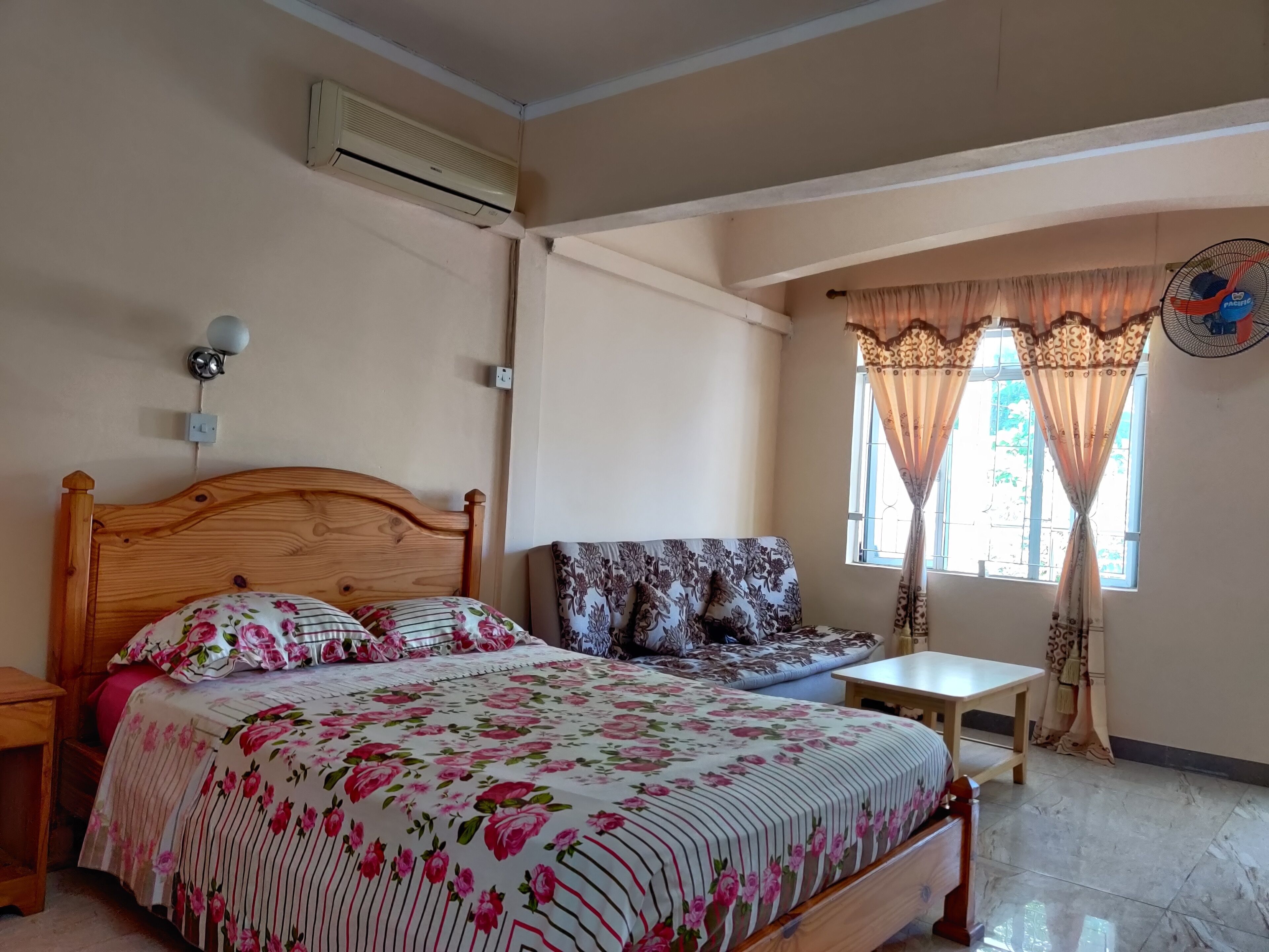 A bedroom with a wooden bed, a sofa, a small table, and a window with curtains.