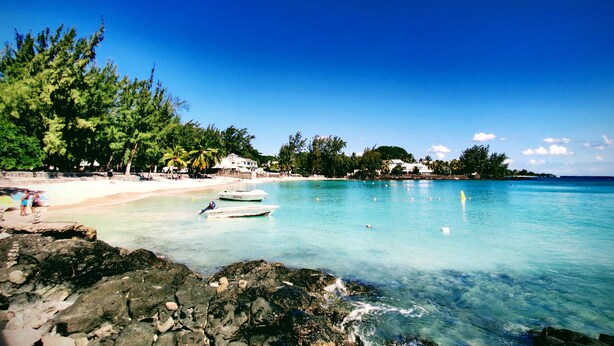 A beach with clear turquoise water, rocky shoreline, and lush greenery. - Pereybere Beach Apartments (Grand-Baie)