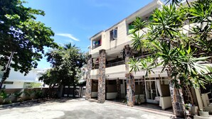 A modern building with a flat roof, multiple balconies, and a covered entrance area with potted plants. - Pereybere Beach Apartments (Grand-Baie)