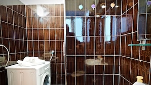 A compact bathroom with a washing machine, a sink, and a mirror.