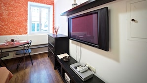 A modern living room with a TV mounted on the wall, a dining table with chairs, and a window with a view of the outside.