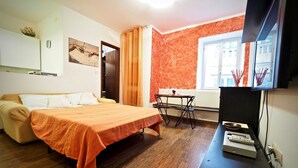 A compact room with a bed, a small table with chairs, a TV, and a window.