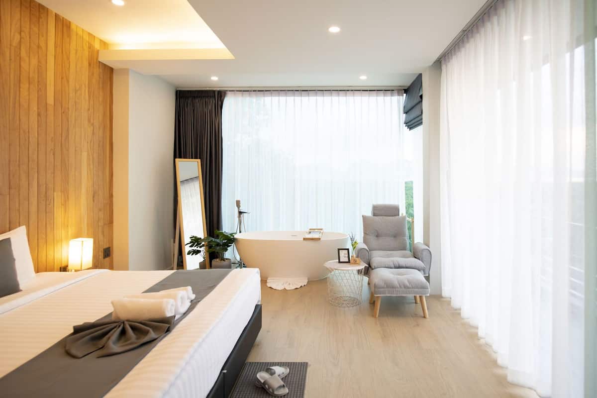 Quarto de hotel moderno com uma cama grande, área de estar com uma poltrona, uma mesa redonda e uma banheira.