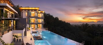 Un edificio moderno de varios pisos con piscina infinita en la azotea y vistas a un paisaje montañoso.