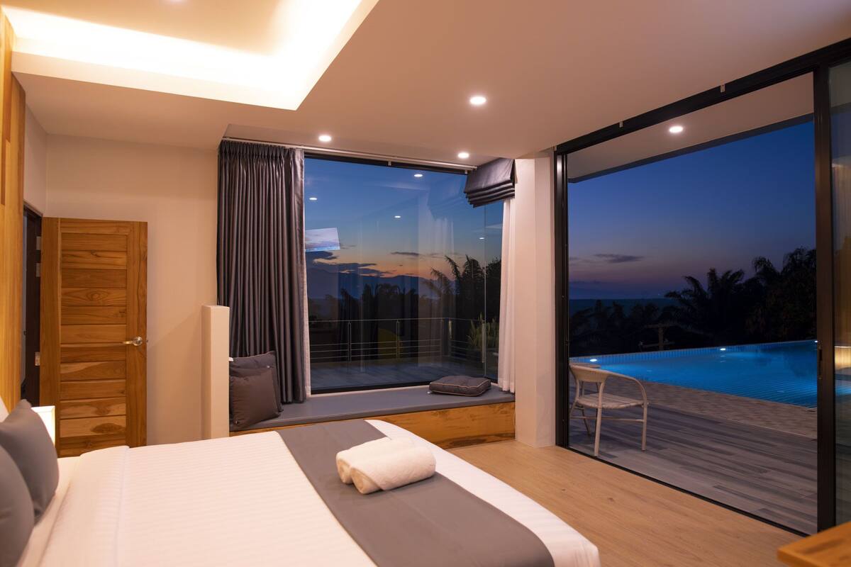 Quarto moderno com cama grande, vista para uma piscina e porta de vidro deslizante para o exterior.