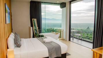 A modern hotel room with a large bed, a painting on the wall, a view of a balcony with outdoor furniture, and a large window.