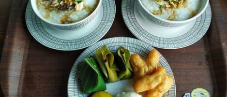 Two bowls of rice porridge with toppings, a plate with vegetables and fried items, and a small dish of white sauce.