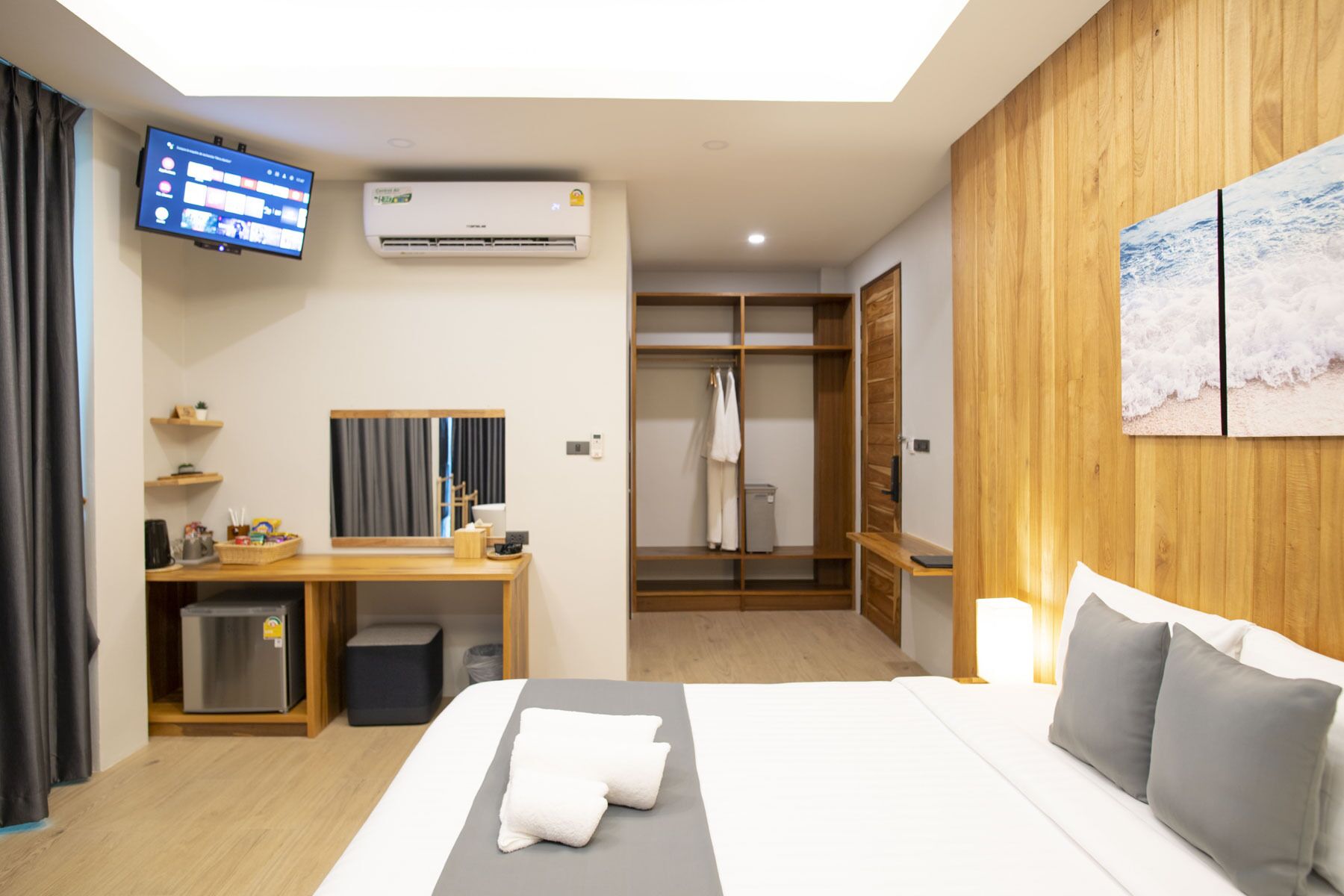 Een hotelkamer met een bed, een bureau, een televisie, airconditioning, een garderobe en een schilderij aan de muur.