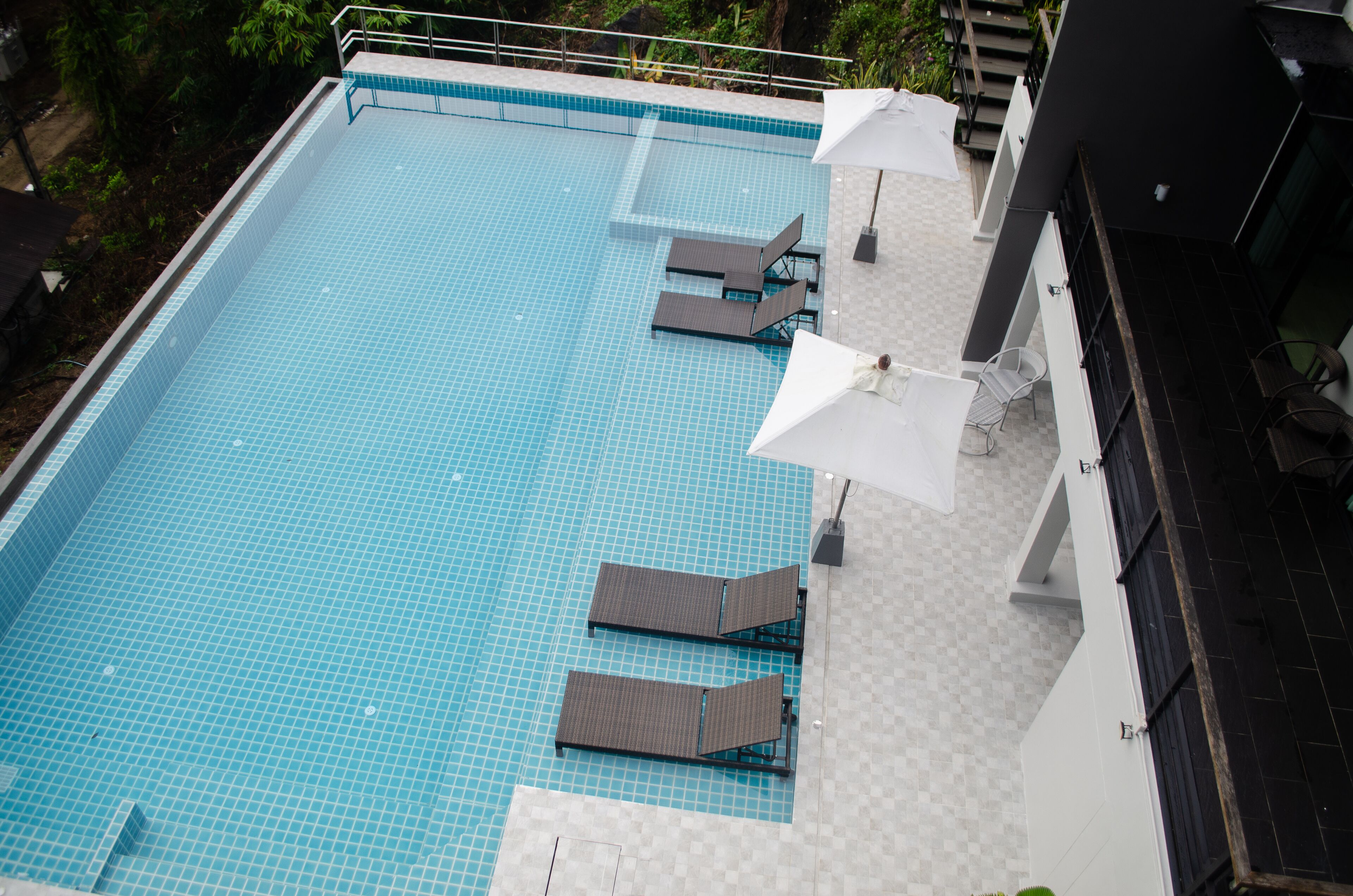 A swimming pool with tiled flooring, lounge chairs, and umbrellas.