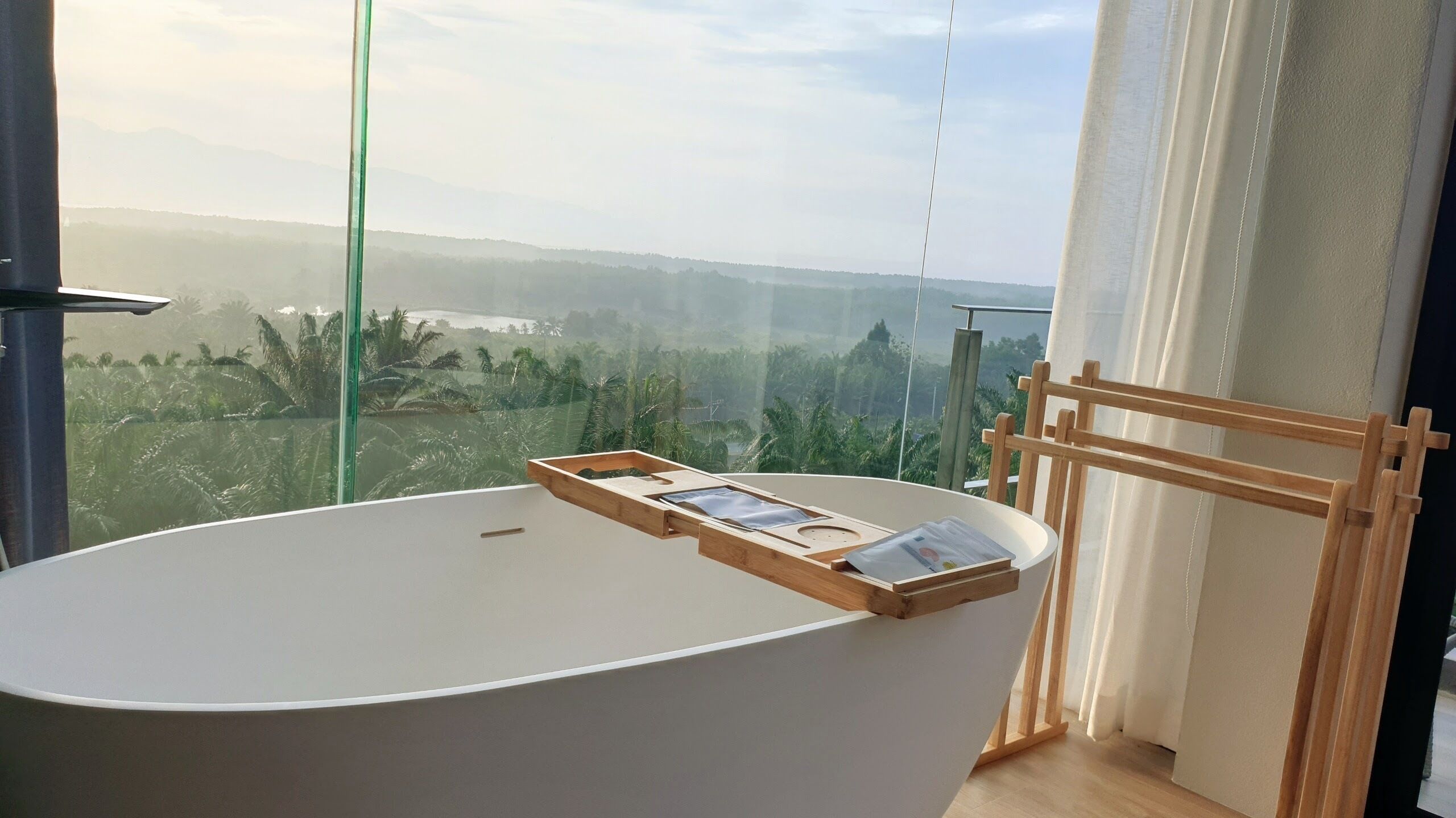 Une salle de bain moderne avec une grande baignoire, une table d’appoint en bois et une vue sur un paysage luxuriant.