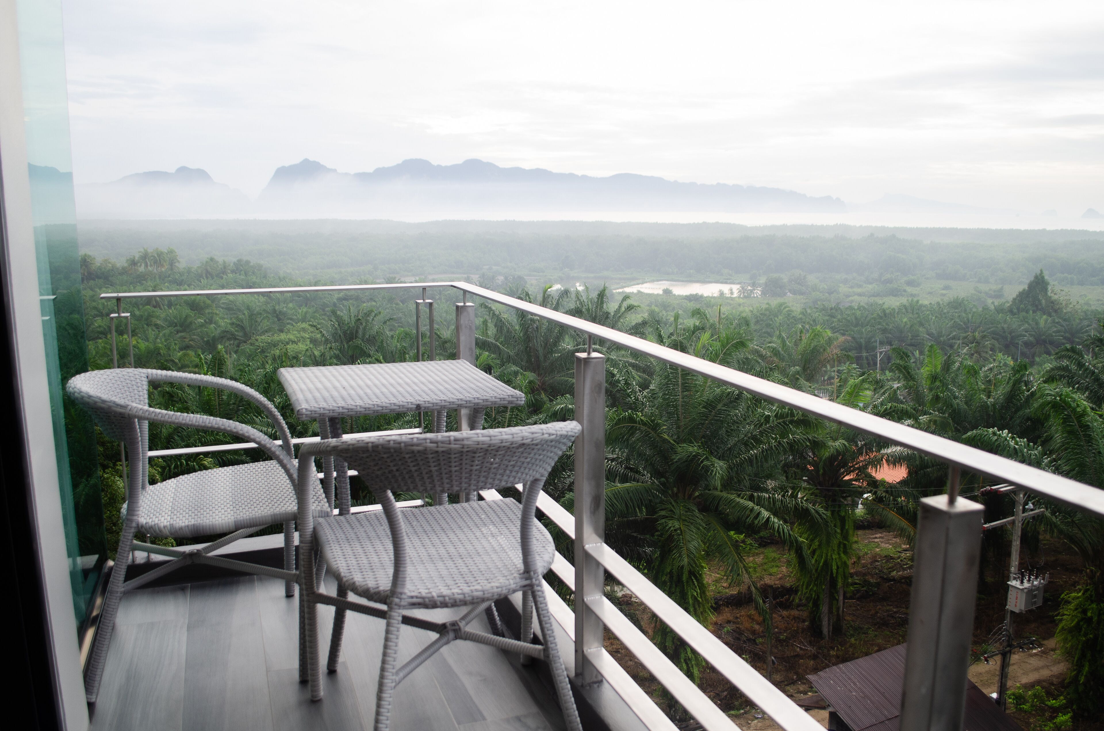 A balcony with wicker furniture overlooking a lush landscape with palm trees and distant mountains.