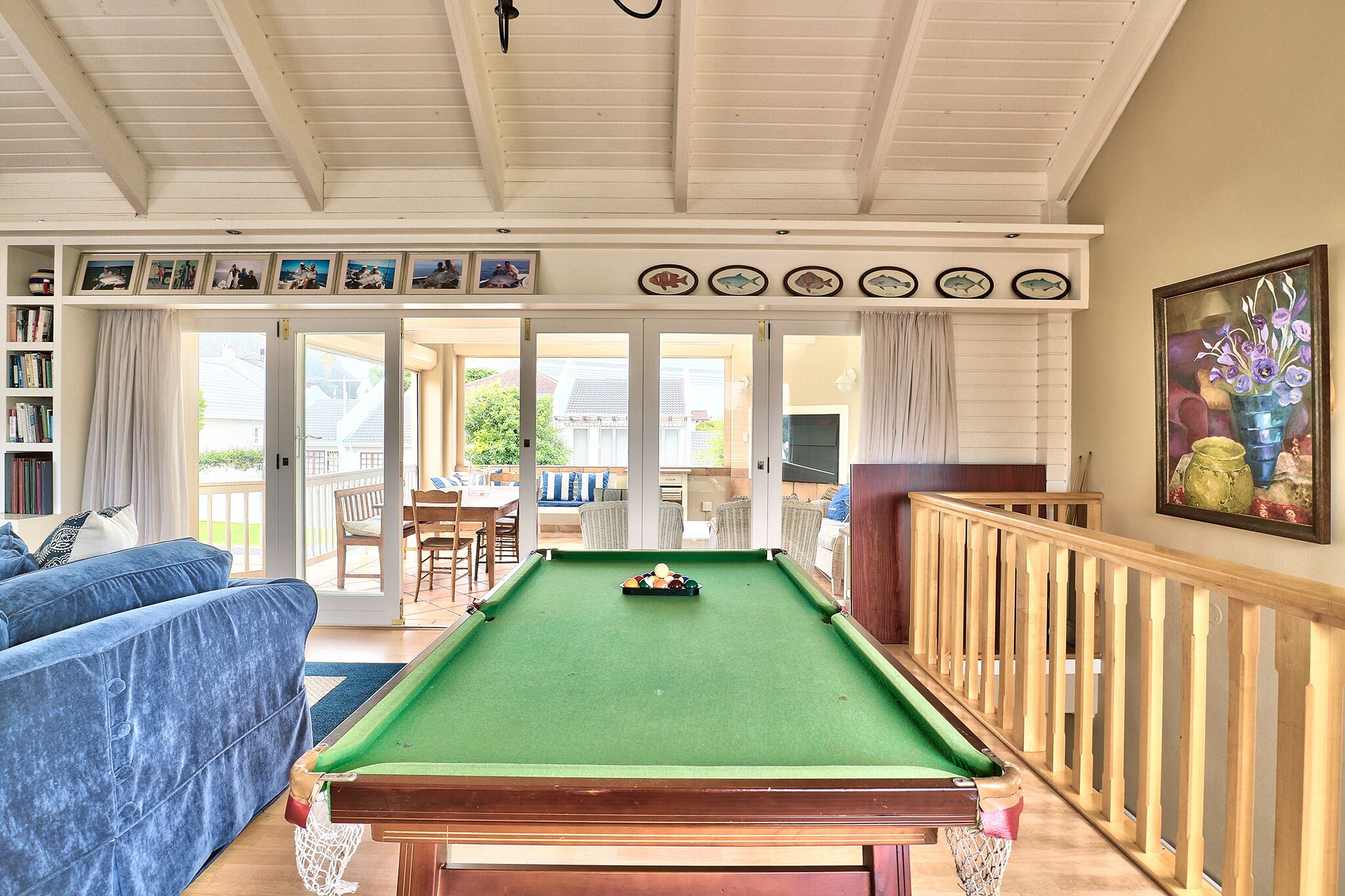 A pool table in a room with a blue sofa, a wooden railing, and a view of the outside.