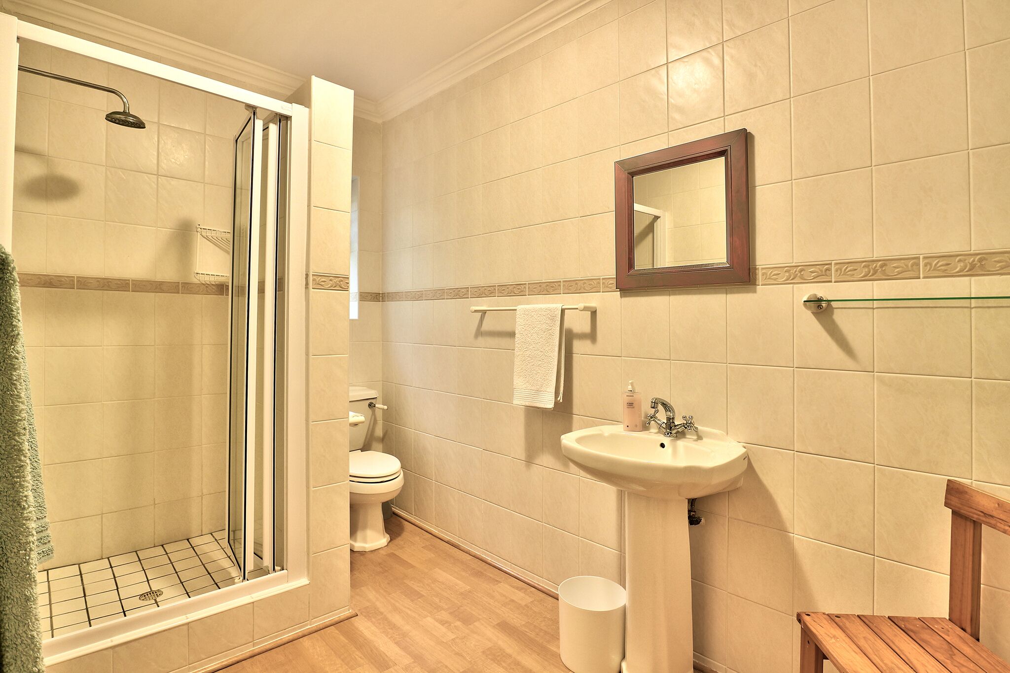 Un baño con cabina de ducha de vidrio, inodoro, lavabo y banco de madera.