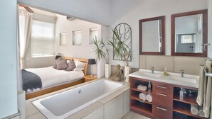 A modern bathroom with a bathtub, a double sink vanity, and a large mirror. - Maudville (Cape Town)