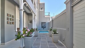 A narrow outdoor corridor with a pool, potted plants, and decorative wall art. - Maudville (Cape Town)