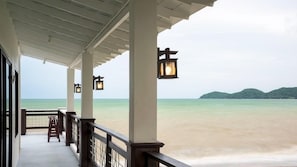 A covered balcony with a view of a beach and distant hills.