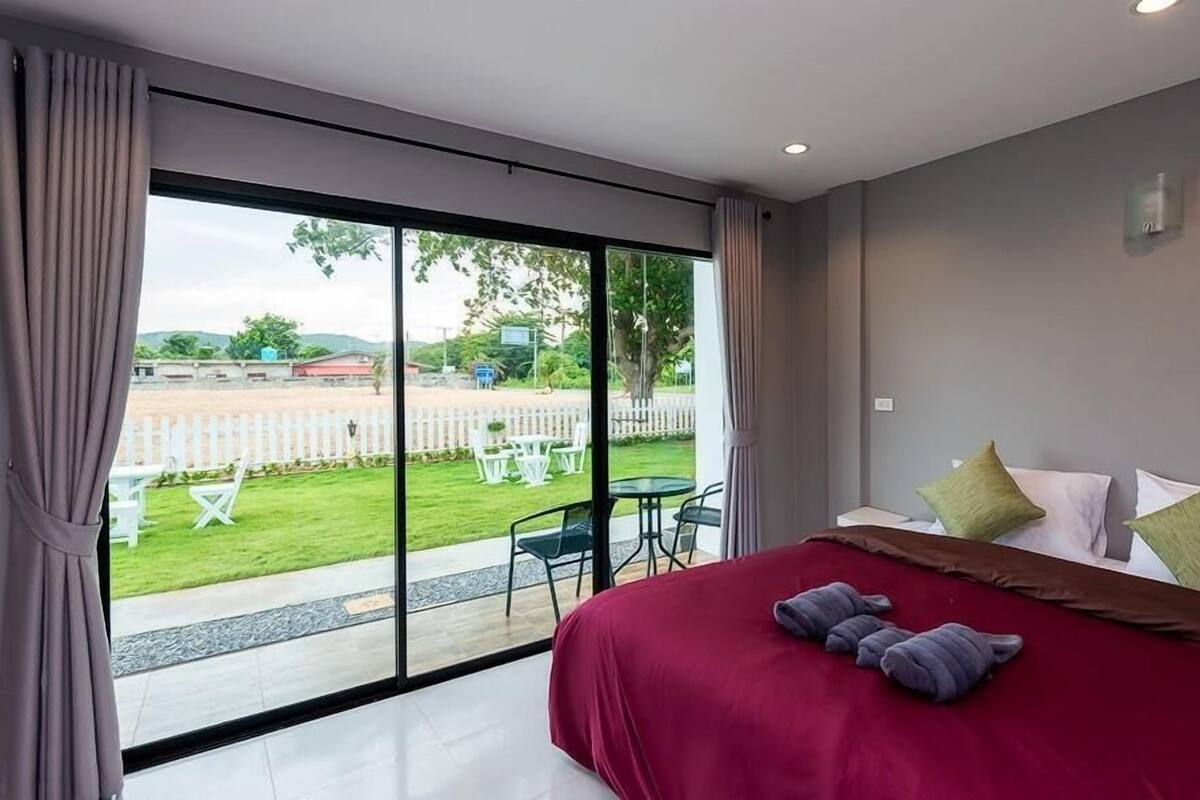 Quarto com cama grande, vista para um jardim e cerca branca.