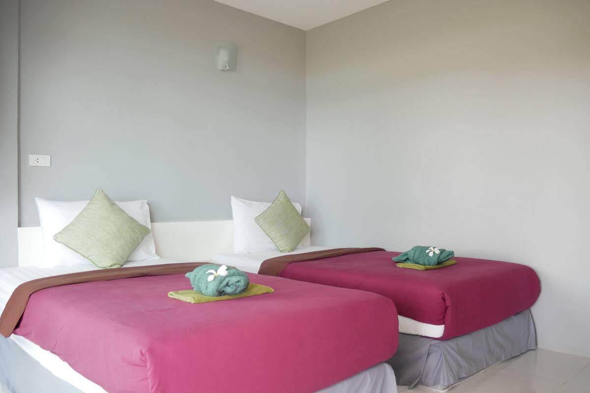 Quarto de hotel com duas camas, cada uma com colcha rosa e almofadas verdes.