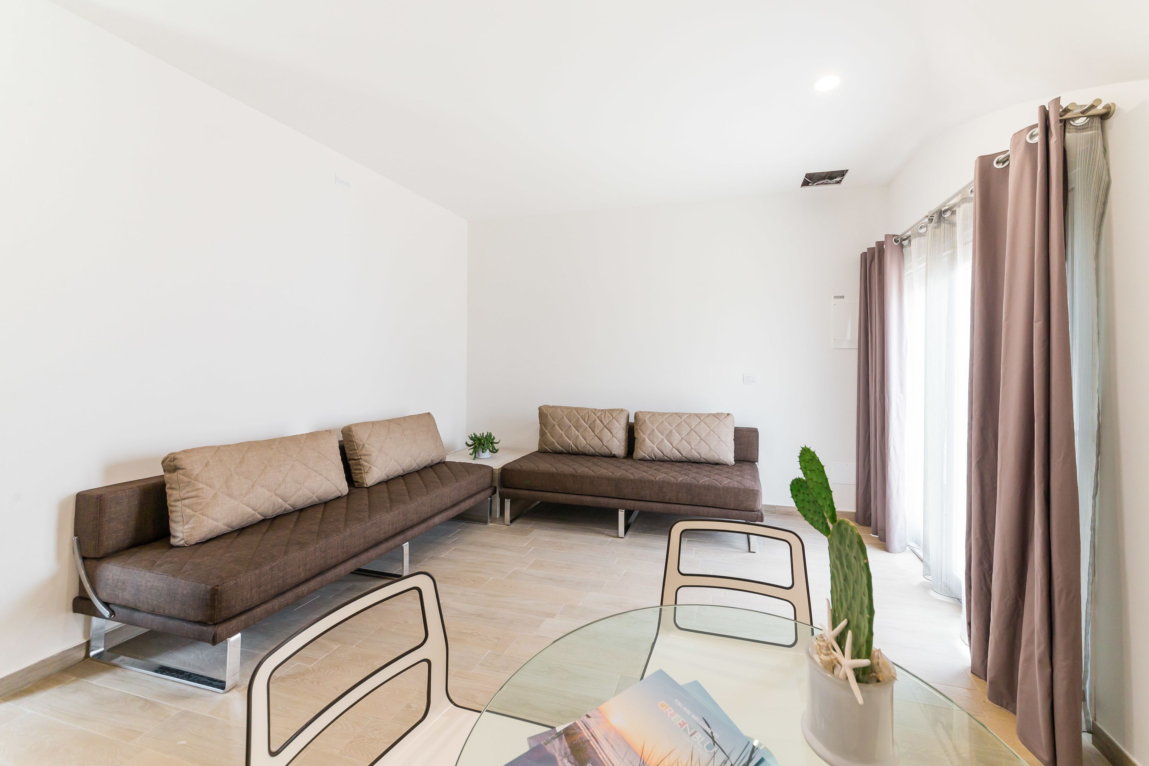 Una sala de estar moderna con un sofá modular, una mesa de centro de vidrio y una planta de cactus.