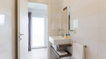 A modern bathroom with a white sink, mirror, and tiled walls.