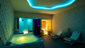 A modern spa room with a large bathtub, two sun loungers, and a small table with a vase.