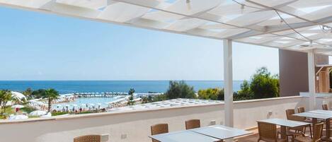 Terraza al aire libre con mesas y sillas, con vista a una playa y al mar.