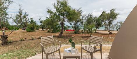 An outdoor seating area with two wooden chairs and a table, surrounded by trees and a view of the sea.