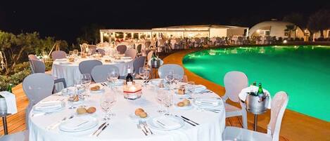 An outdoor dining area with round tables set for a meal, surrounded by a pool.
