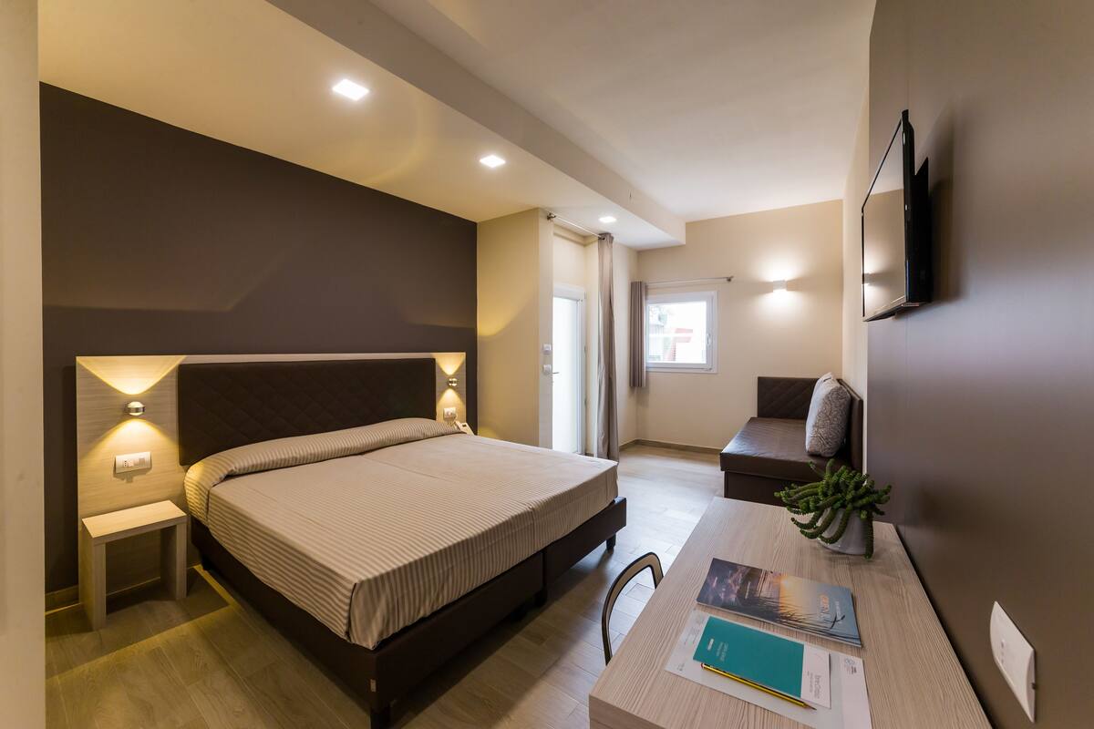 A modern hotel room with a large bed, bedside tables, a desk, and a TV mounted on the wall.